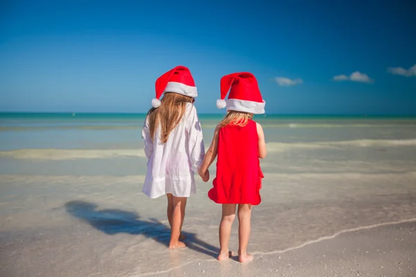 Two little cute girls in Christmas hats have fun on the exotic beach — Zdjęcie stockowe